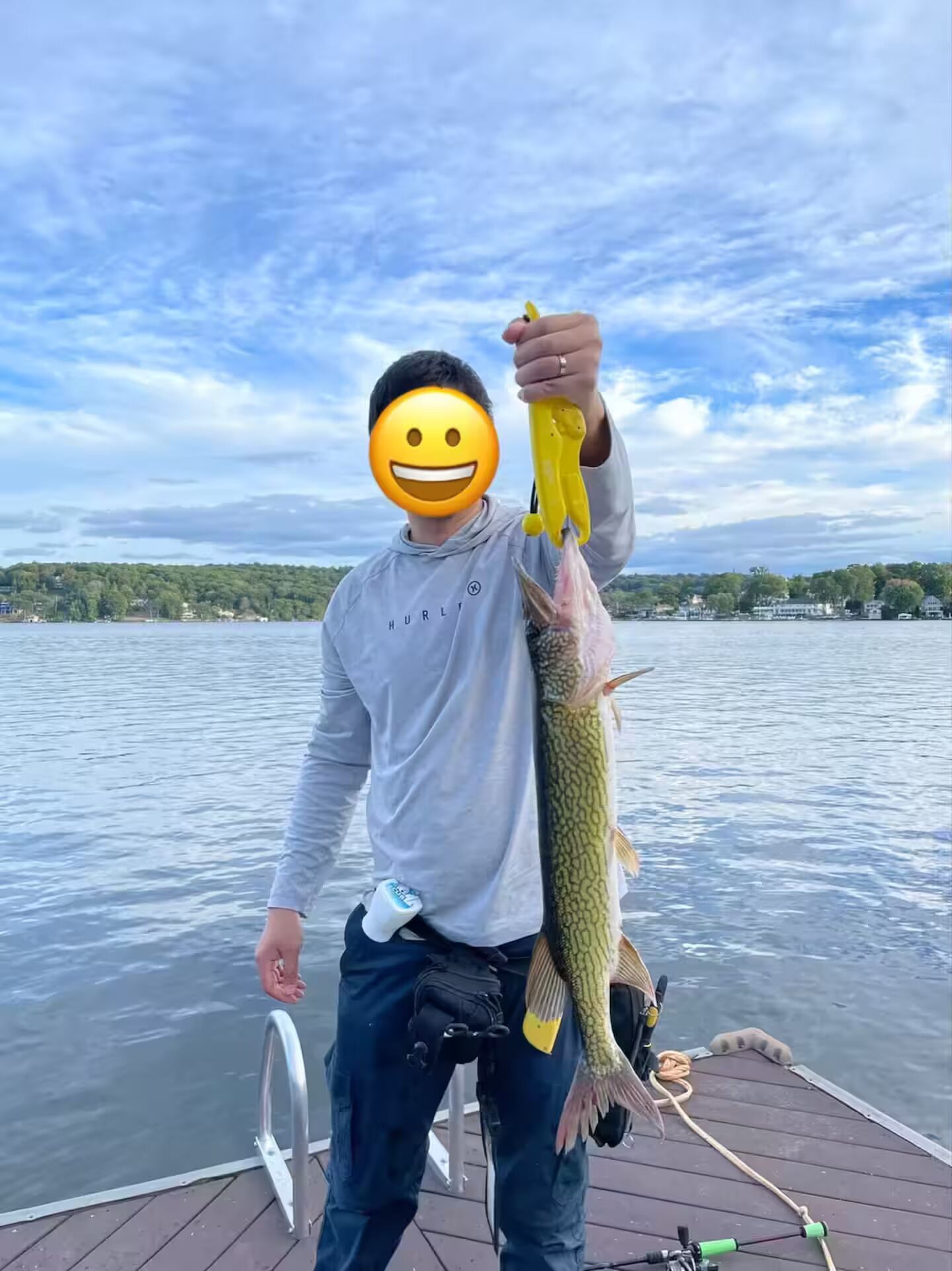 A person holding a fish on a boat with a lake and trees in the background.