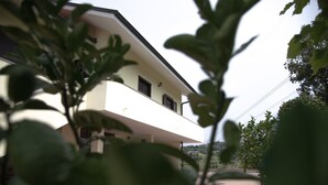 Um edifício de dois andares com varanda, rodeado por vegetação.