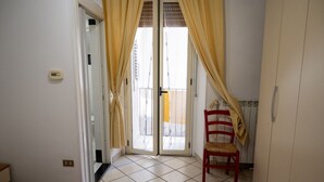 Ein Zimmer mit einem Bett, einem Sessel, einem Kleiderschrank und einer Glastür zum Balkon.
