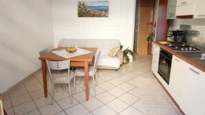 Eine kleine Küche mit Esstisch und Stühlen, einem Sofa, einem Bild an der Wand und einer Uhr.