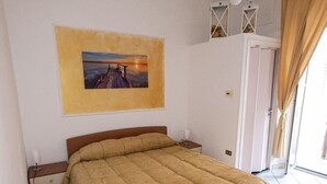 Ein Schlafzimmer mit Bett, einem Bild an der Wand, einem Nachttisch und einer Tür, die auf einen Balkon führt.