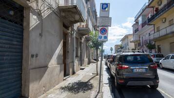 Une rue étroite bordée de voitures garées, une porte de garage bleue et un bâtiment sur lequel est apposée une enseigne indiquant un espace de stationnement.