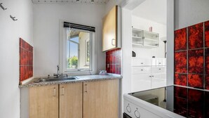 Una cocina con armarios de madera, un lavamanos de acero inoxidable, una ventana y un salpicadero con azulejos rojos.