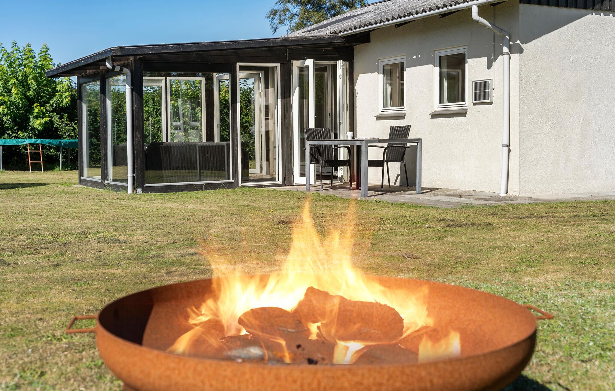 A backyard with a fire pit, a covered patio, and a house with a white exterior.