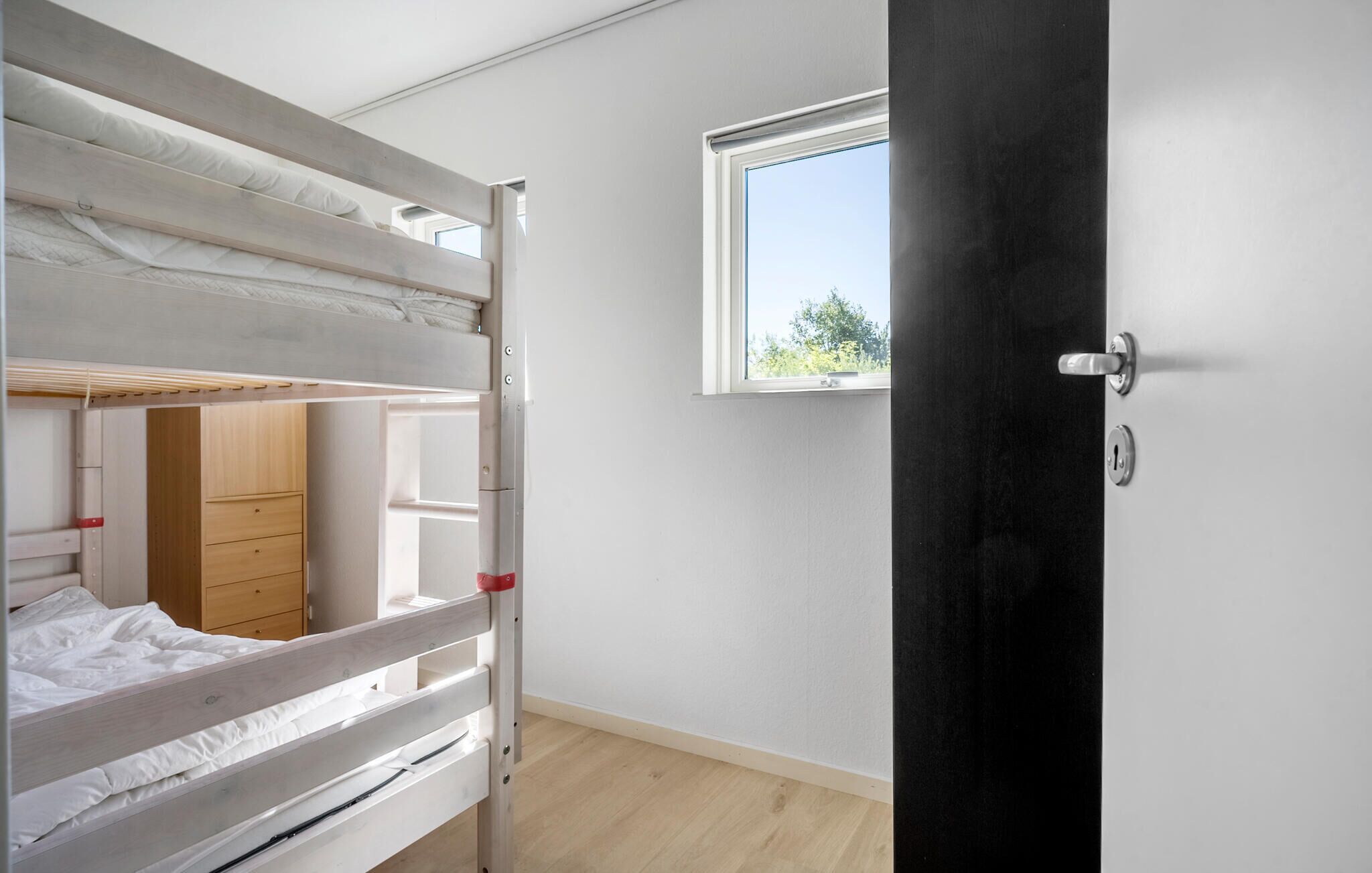 Una camera da letto con un letto a castello, un'armadio in legno, una finestra vista su del verde e una porta con serratura.