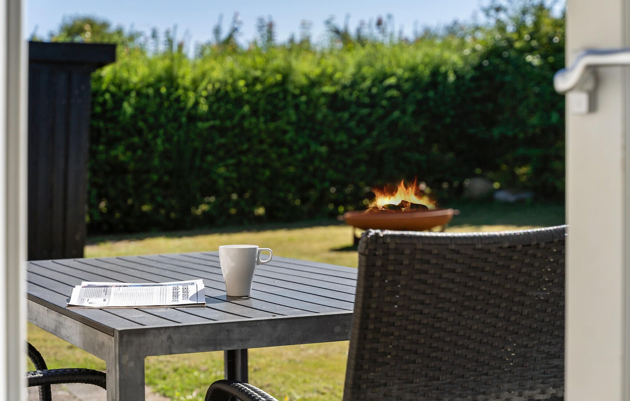 Una mesa de patio con un periódico, una taza blanca y un brasero encendido.