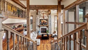 A spacious living area with a fireplace, wooden beams, and a staircase.