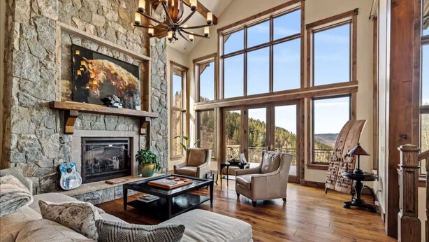 A spacious living room with a stone fireplace, large windows, and a view of the outdoors.