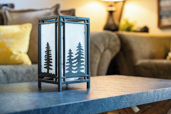 A metal lantern with tree designs on a wooden table in a living room.