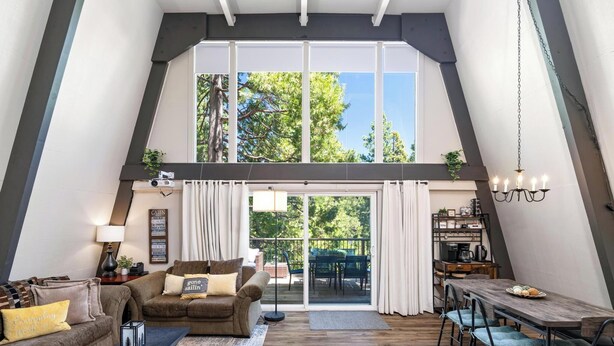 A spacious loft-style living area with a high ceiling, a dining table, and a sliding glass door leading to an outdoor patio.
