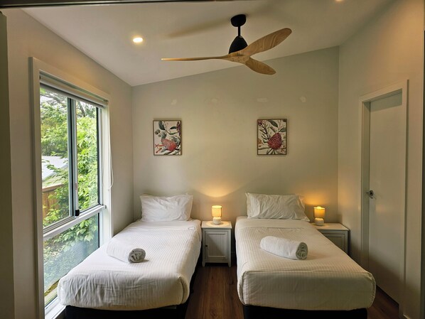 A bedroom with two beds, a ceiling fan, and artwork on the walls.