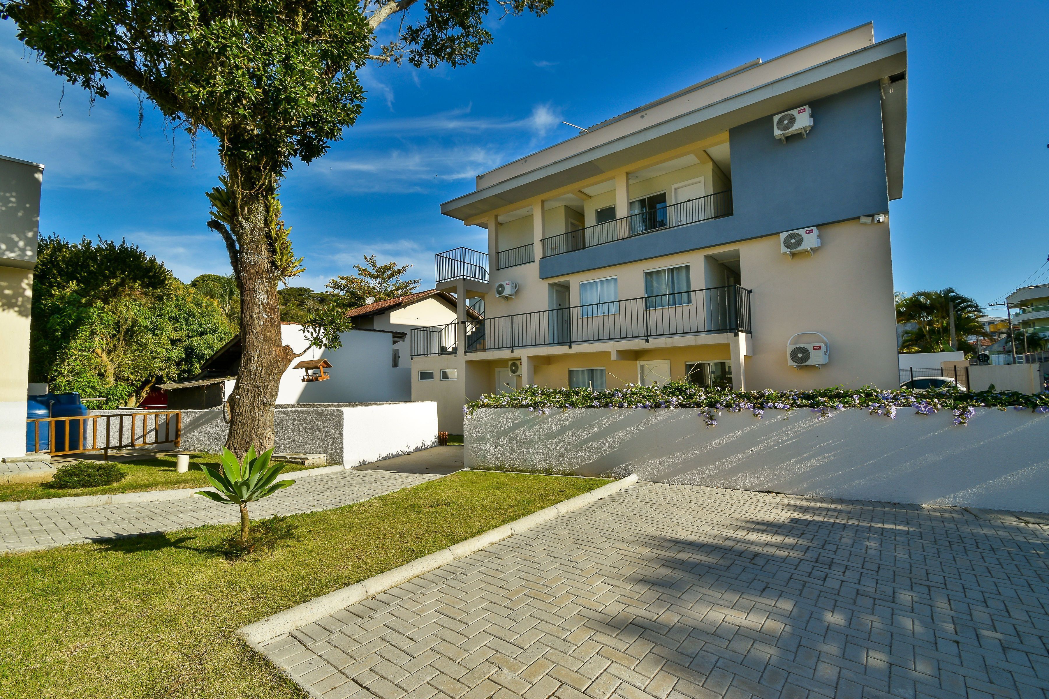 A modern multi-story building with balconies, air conditioning units, and a paved driveway.