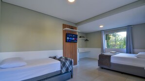 A hotel room with two beds, a TV mounted on the wall, a window with curtains, and a small shelf with a towel. - Mar de Bombinhas - Centro (Bombinhas)