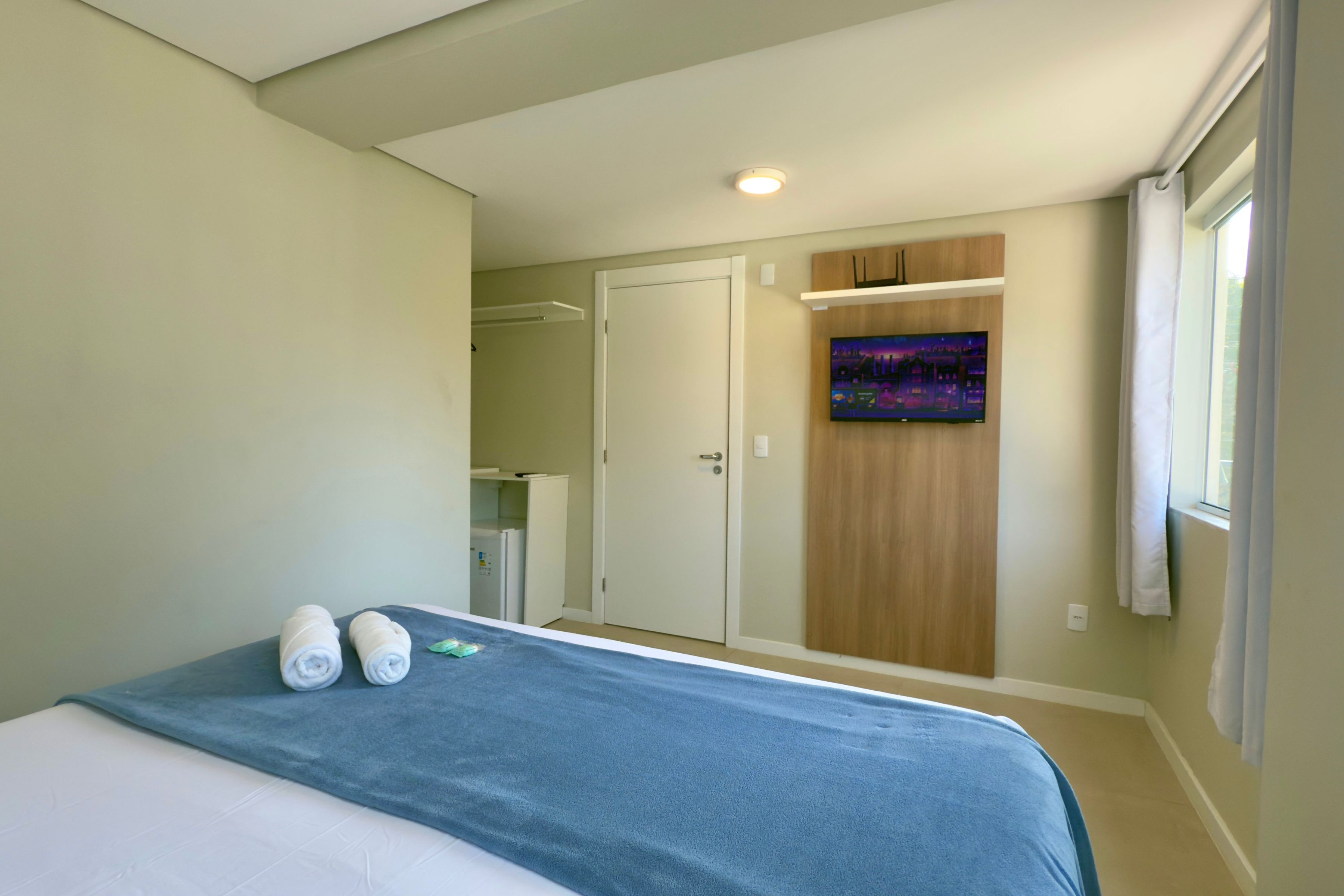A hotel room with a bed, a bathroom, and a TV on the wall.