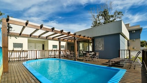 A swimming pool with wooden deck, outdoor seating, and a pergola structure. - Mar de Bombinhas - Centro (Bombinhas)