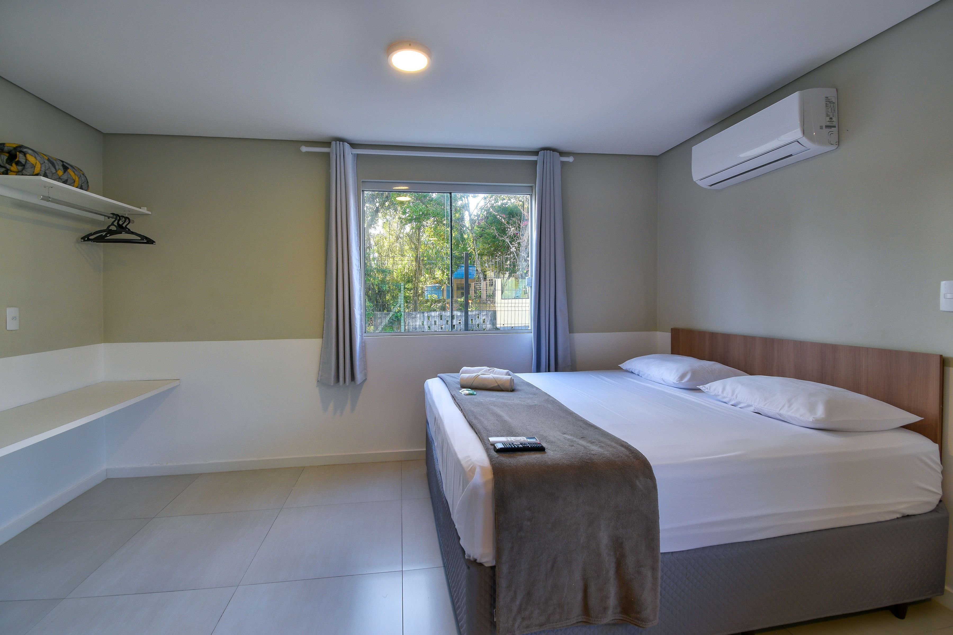 Una habitación de hotel moderna con una cama grande, una mesita de noche, una ventana con cortinas, un equipo de aire acondicionado y vistas al exterior.