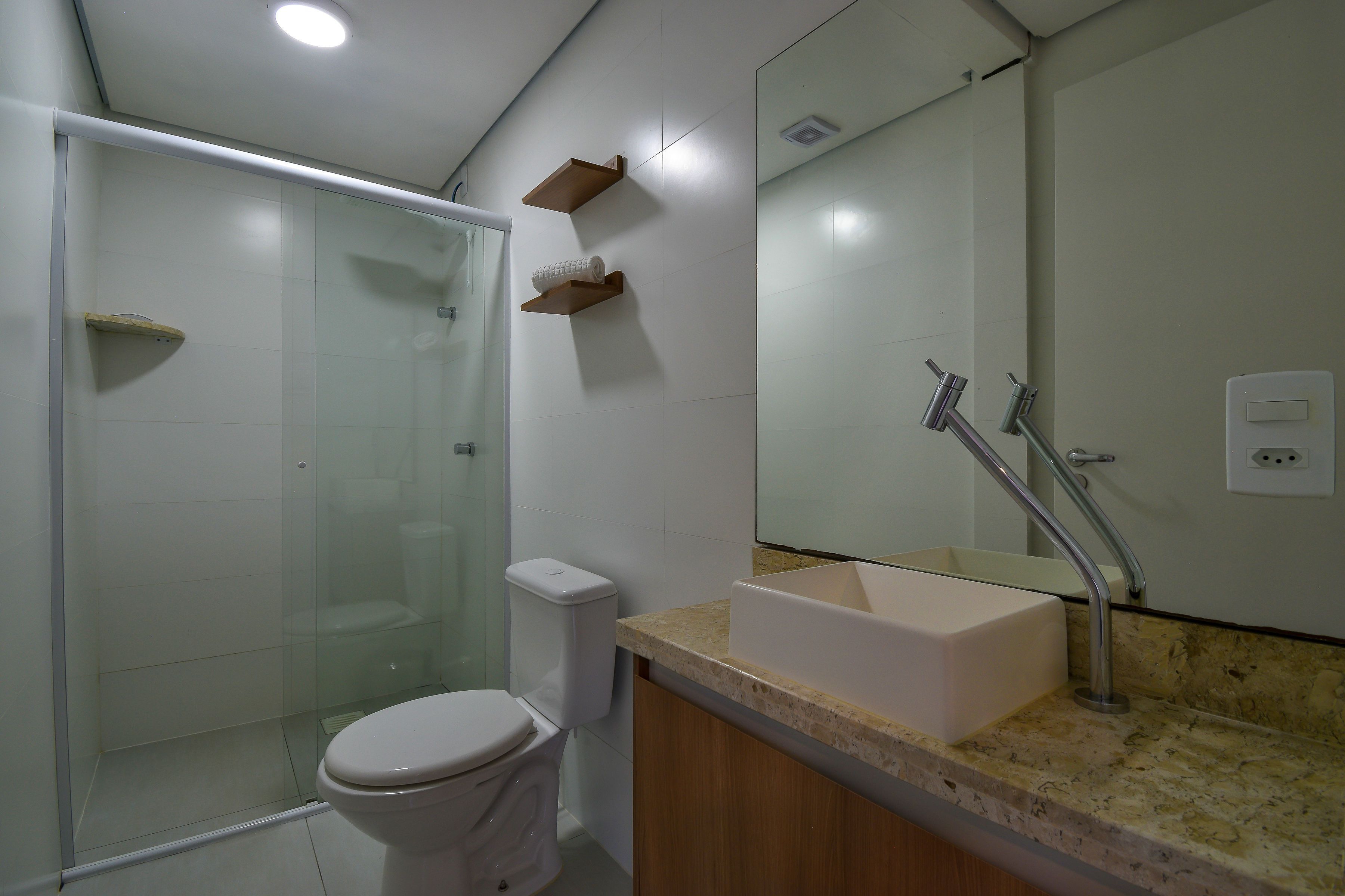 A modern bathroom with a glass shower enclosure, a toilet, a sink with a marble countertop, and a mirror.