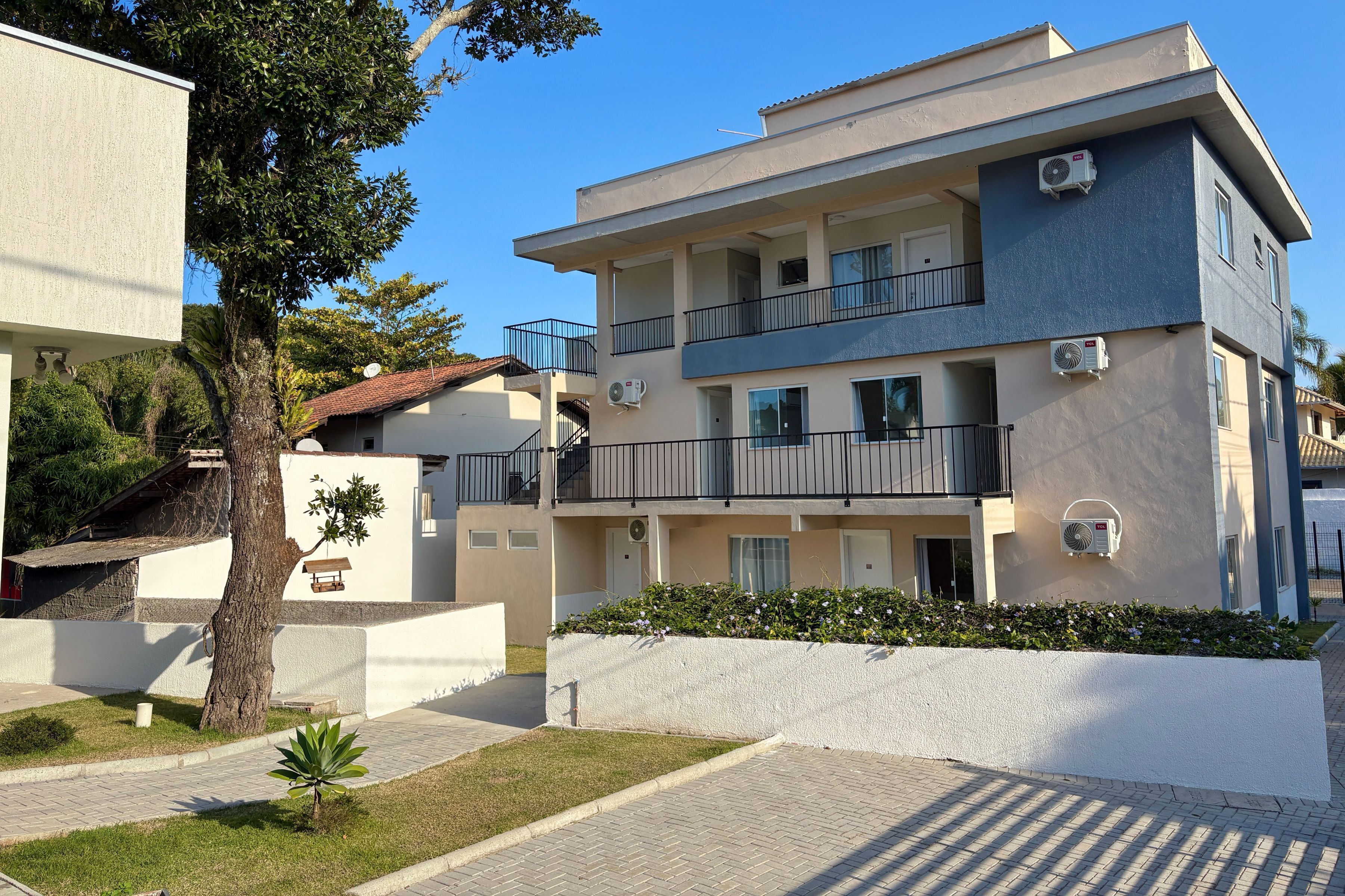 A multi-story residential building with balconies, air conditioning units, and a small garden area.