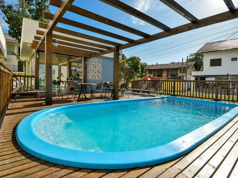 Una terraza de madera con un jacuzzi, mobiliario exterior y una pérgola.