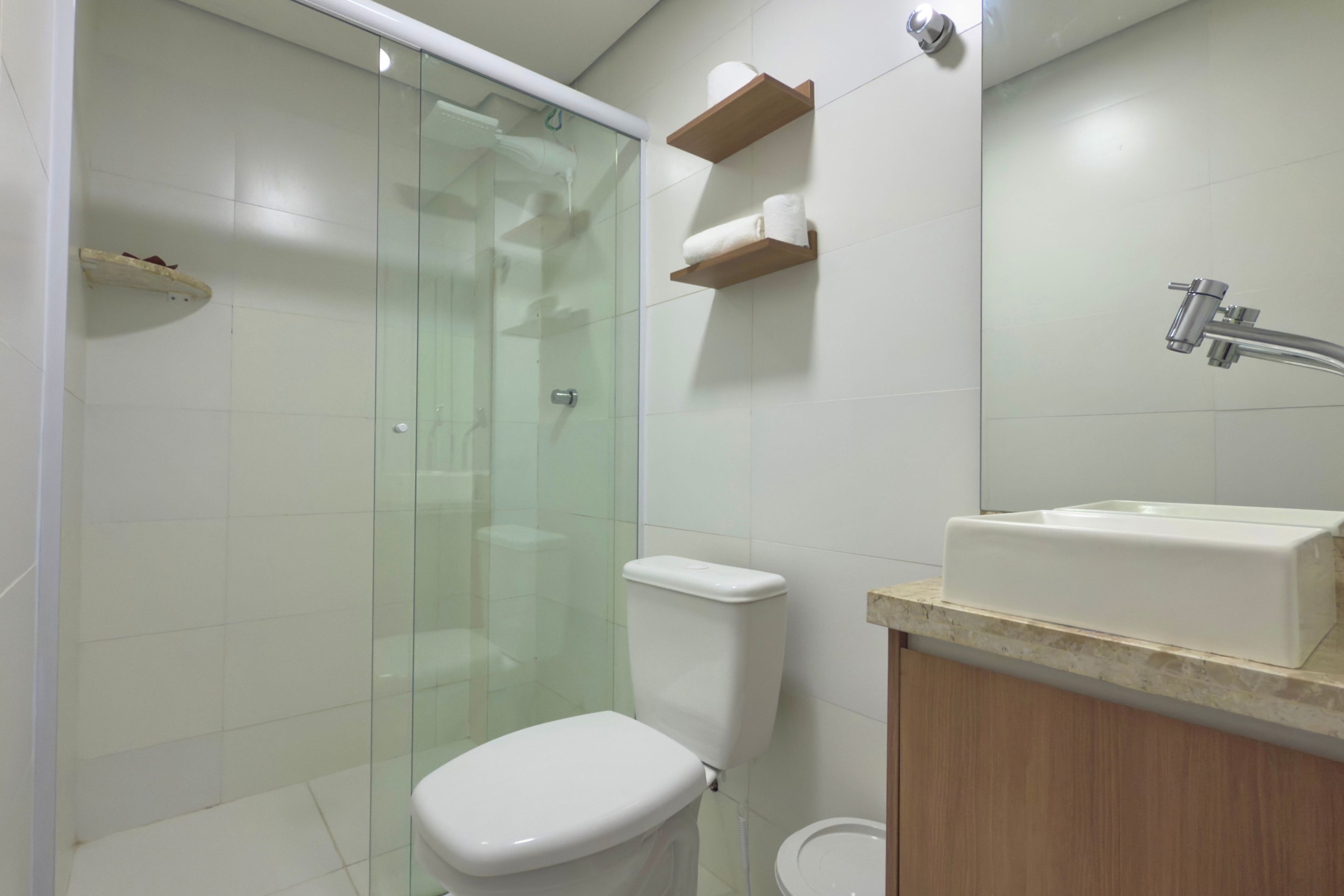 Un baño moderno con ducha envuelta en vidrio, inodoro y lavamanos con encimera de madera.