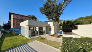 A modern building with a glass facade, a paved courtyard, and a small garden area. - Mar de Bombinhas - Centro (Bombinhas)