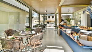 A modern indoor dining area with wicker chairs, a glass table, and a buffet counter with various food items. - Mar de Bombinhas - Centro (Bombinhas)