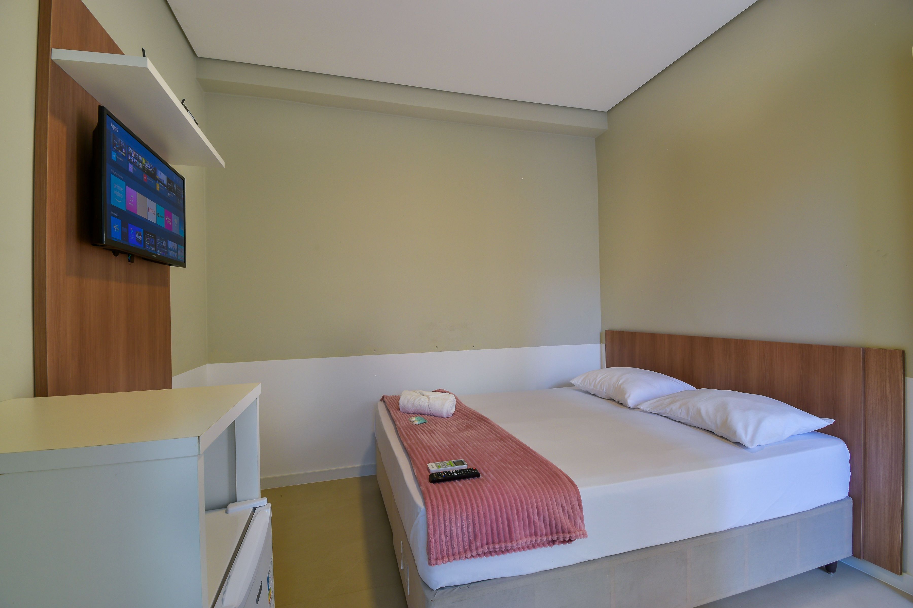 Een hotelkamer met een bed, een aan de muur bevestigde televisie en een bureau met een stoel.
