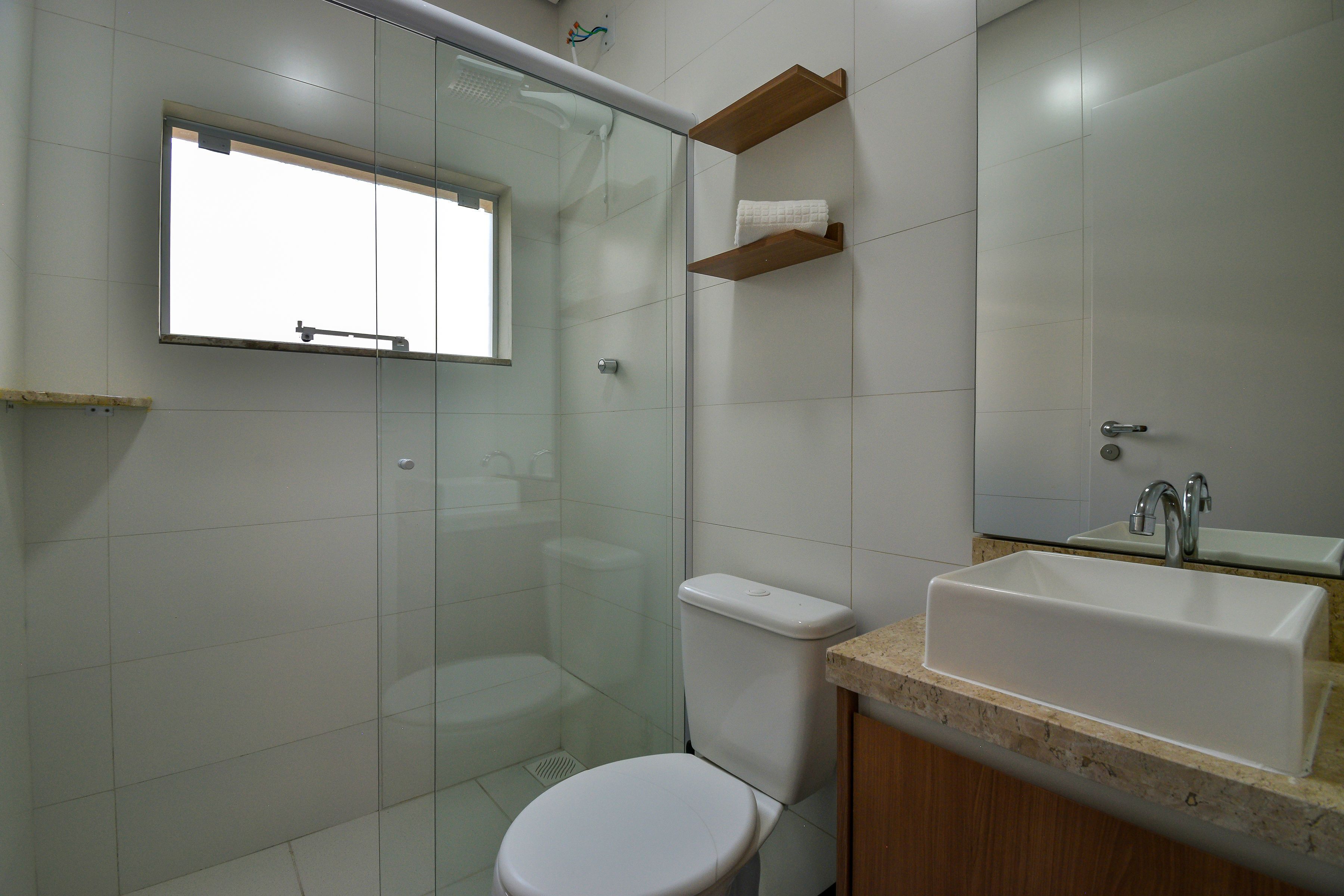 Ein Badezimmer mit Duschkabine, weißer Toilette, Waschbecken mit Spiegel und Ablage für Handtücher.