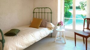 A single bed with a green metal frame, a small round table with a vase of flowers, and a wooden chair. - LARGETEAU astronomer's house (Mouilleron Saint Germa)