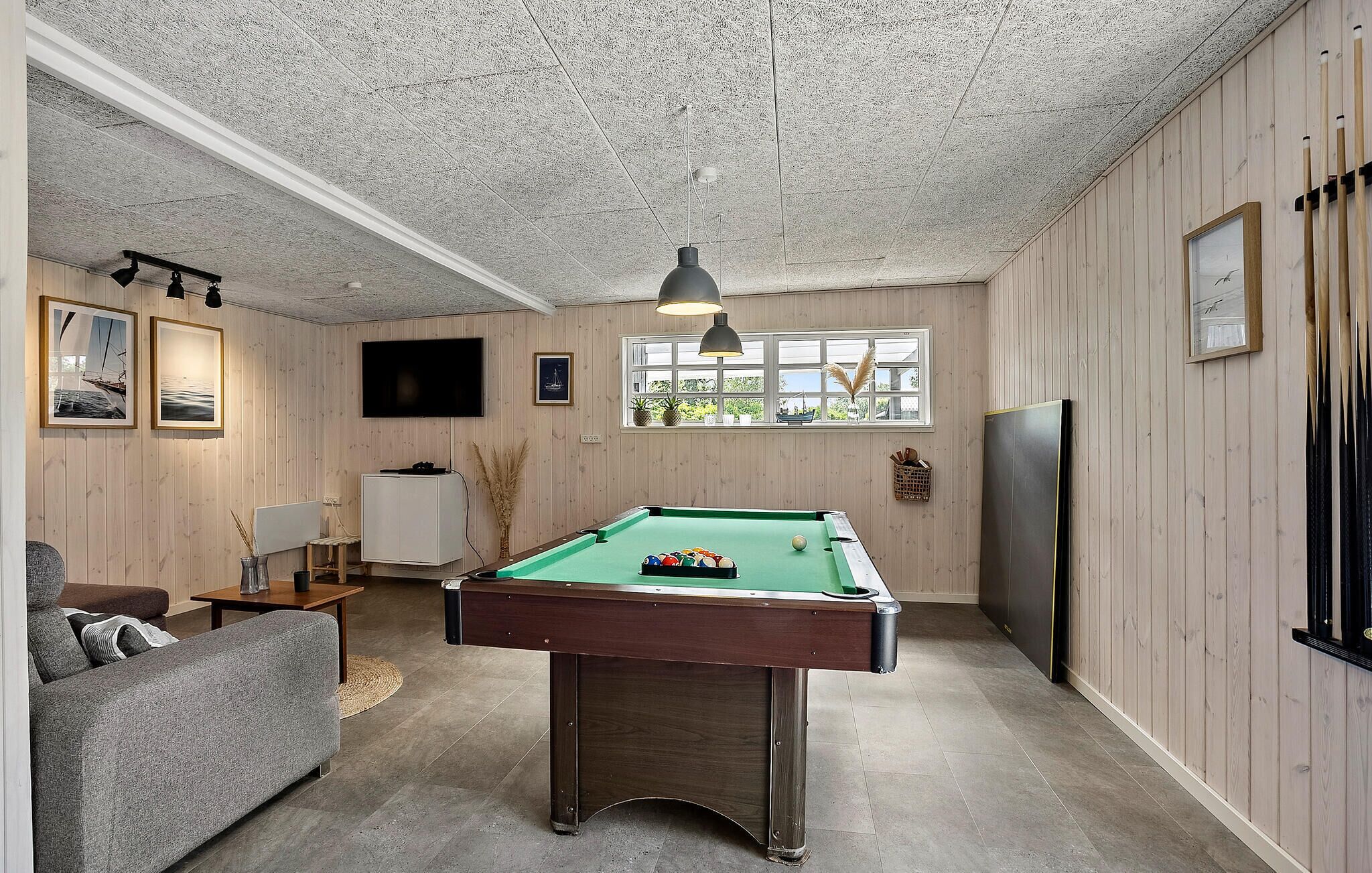 A pool table in a room with wooden walls, a television, and framed pictures.