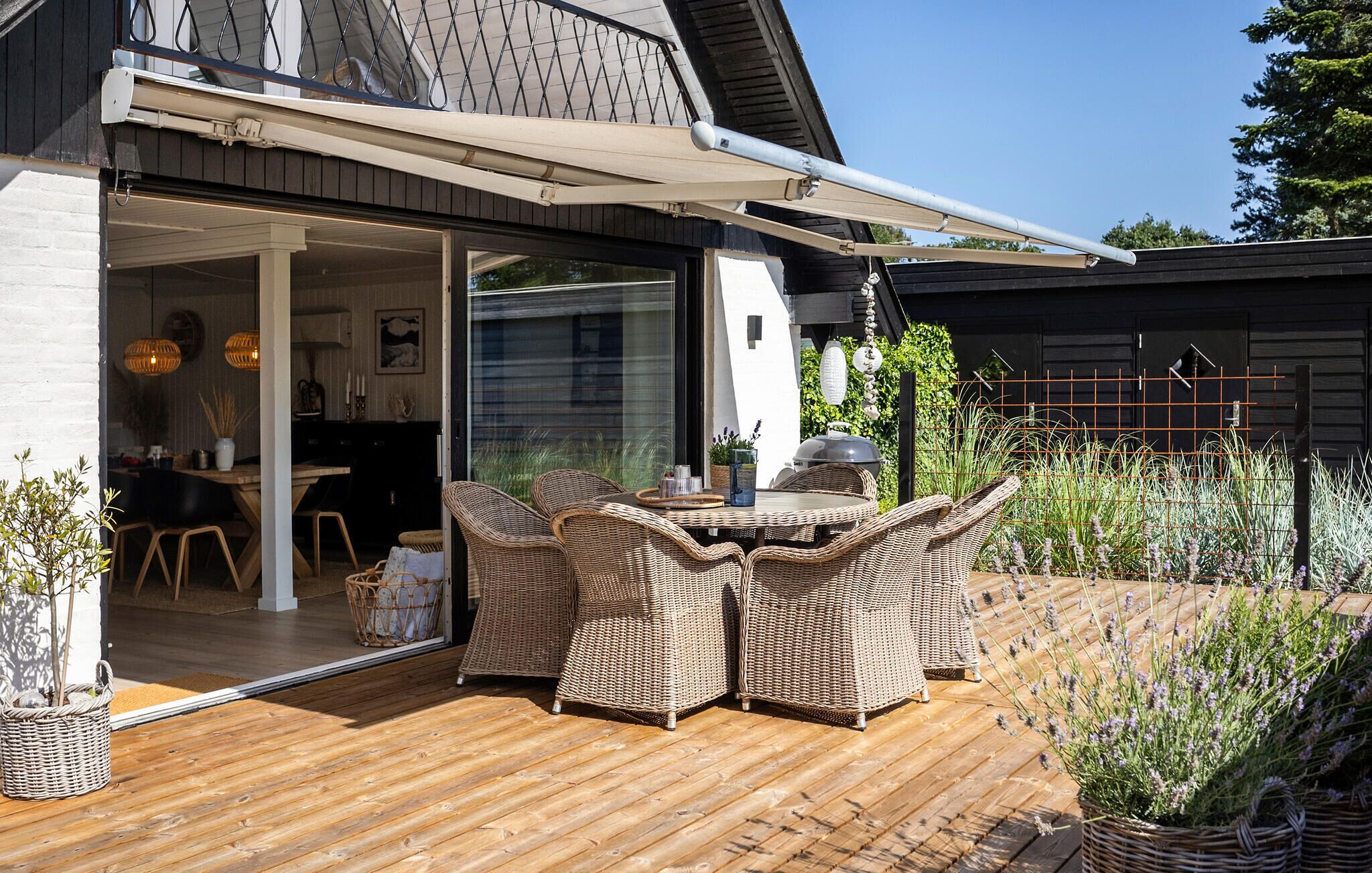 Een terras buiten met rieten meubels, een tafel en een barbecue.