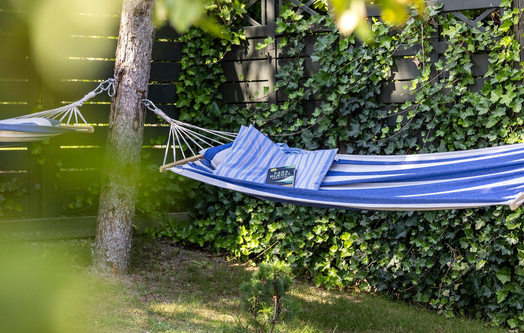 A hammock tied to a tree in a garden with a wooden fence and ivy-covered wall in the background.