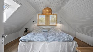 A bedroom with a sloped ceiling, a bed with striped bedding, a hanging rattan light fixture, and a window with blinds.