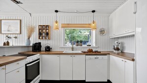 A modern kitchen with white cabinetry, a wooden countertop, a built-in oven, and a window with a view of greenery.