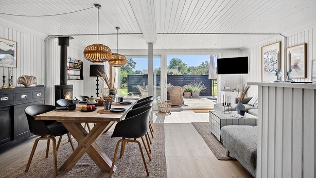 A modern kitchen with a dining area, featuring a wooden table, black chairs, and a large window overlooking a garden.