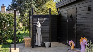 A wooden outdoor area with a door, a hanging towel, a wooden bench, and a metal bucket.