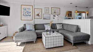 A modern living room with a grey sectional sofa, a white tiled coffee table, and framed artwork on the walls.