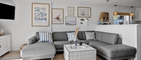 Un salon moderne avec un canapé d’angle gris, une table basse recouverte de carreaux blancs et des œuvres d’art encadrées accrochées aux murs.