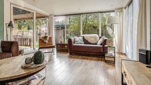 A spacious living room with a brown leather sofa, a wooden coffee table, and a large window offering a view of the outdoors.