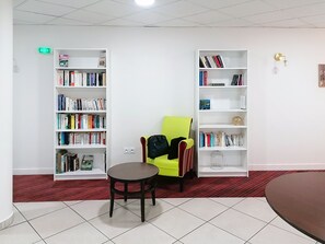 A room with two white bookshelves, a bright yellow chair, a small round table, and a red carpeted floor.