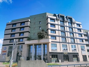 Un immeuble à plusieurs étages doté d’une architecture moderne, caractérisé par de grandes fenêtres et une façade texturée de couleur verte.