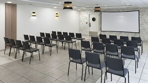 Une salle de conférence avec des rangées de chaises, un écran de projection et un tableau blanc.