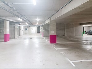 Een meerlaagse parkeergarage met betonnen pilaren, aangeduid parkeerplaatsen en verlichting boven de auto's.