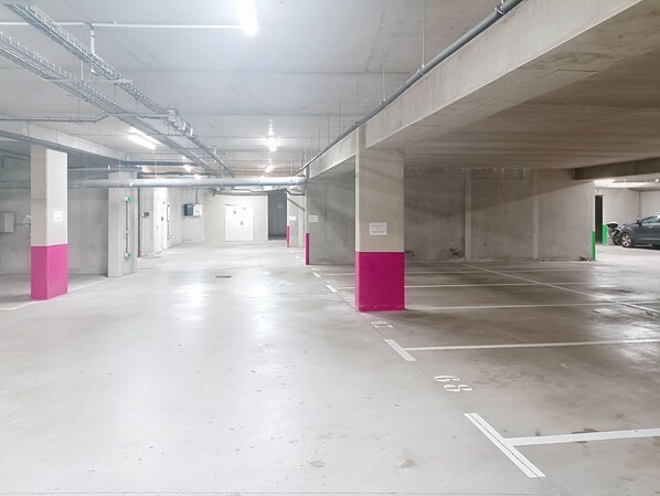 A multi-level parking garage with concrete pillars, marked parking spaces, and overhead lighting.