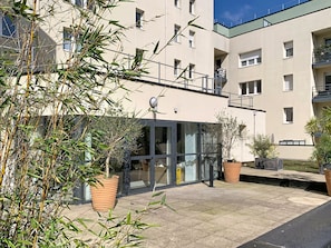 A modern building with a glass entrance, potted plants, and a tiled patio area.