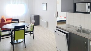 Un espace de vie compact comprenant un coin repas, une kitchenette et un lit à l’arrière-plan.