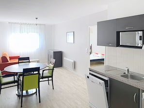 Un espace de vie compact comprenant un coin repas, une kitchenette et un lit à l’arrière-plan.