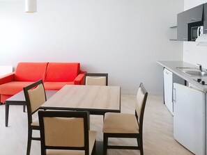 A compact living space with a kitchenette, a dining table with chairs, and a red sofa.