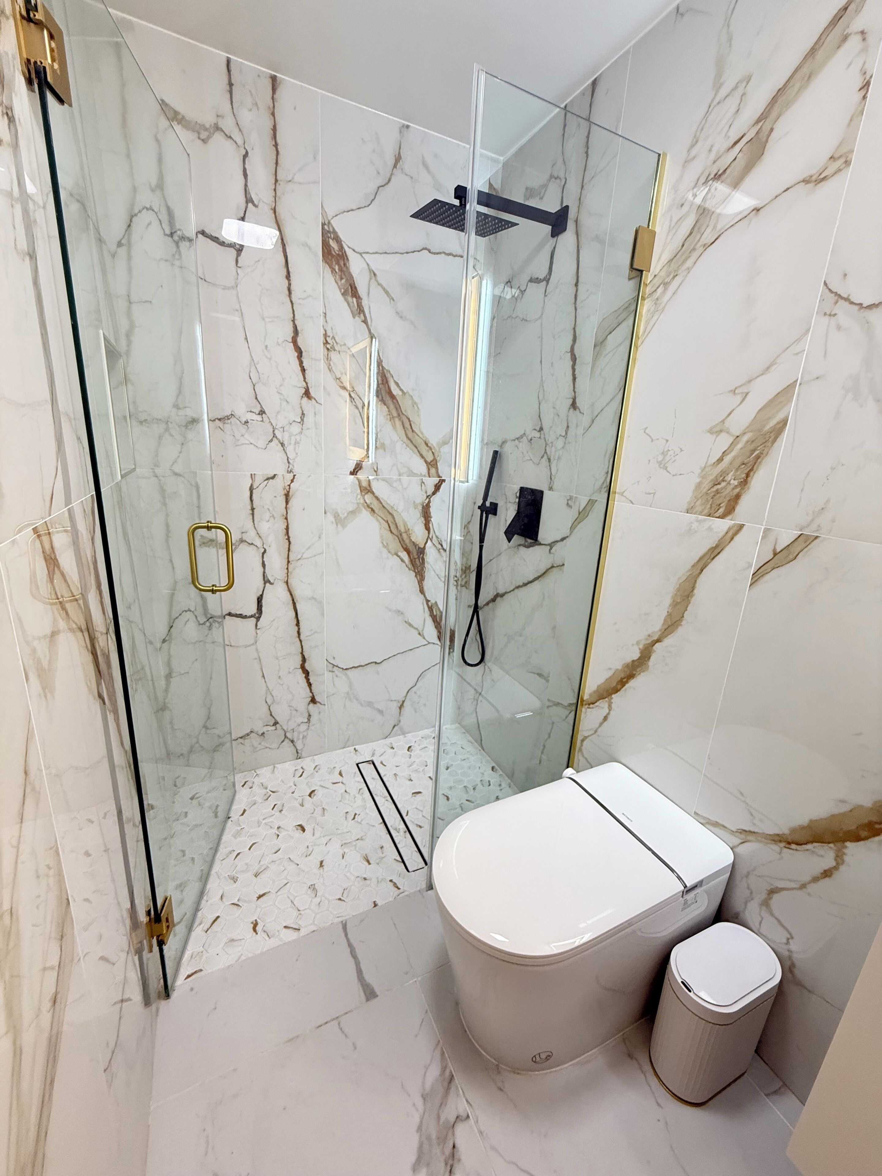 Un bagno moderno con doccia vetro, un water e un cestino.