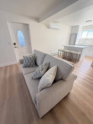 A modern living room with a grey sofa, patterned cushions, and a wooden floor. - Modern 2BR apartment Elmont NY (Elmont)